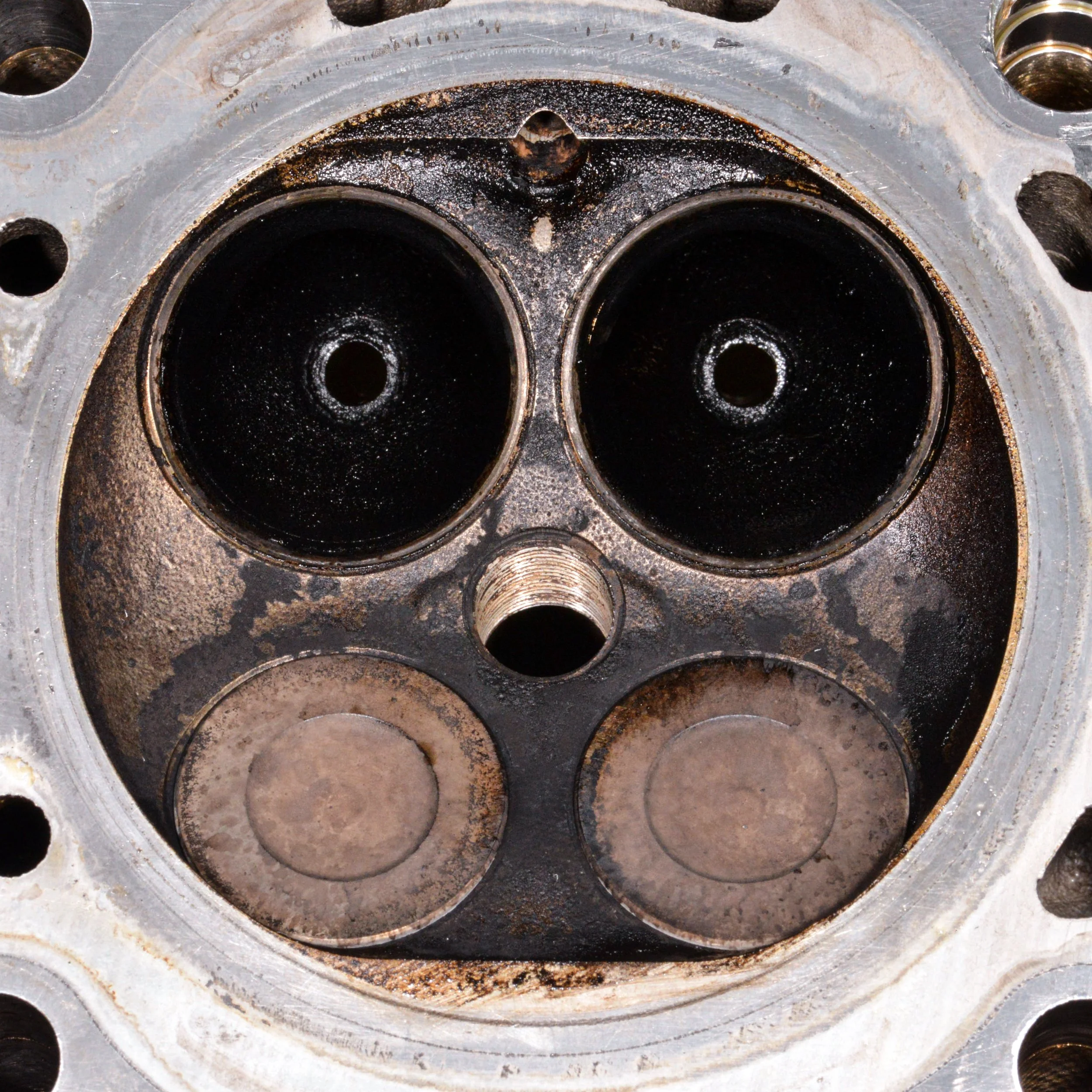 Close-up of an engine cylinder head showing two intake valves, two exhaust valves, and the spark plug hole.