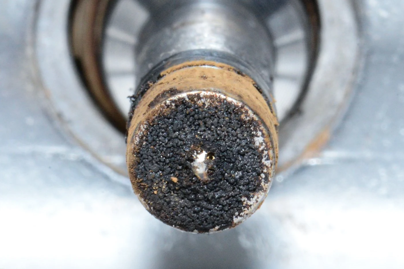 Close-up of a rusted and dirty metal shaft or pipe with black residue at the end.