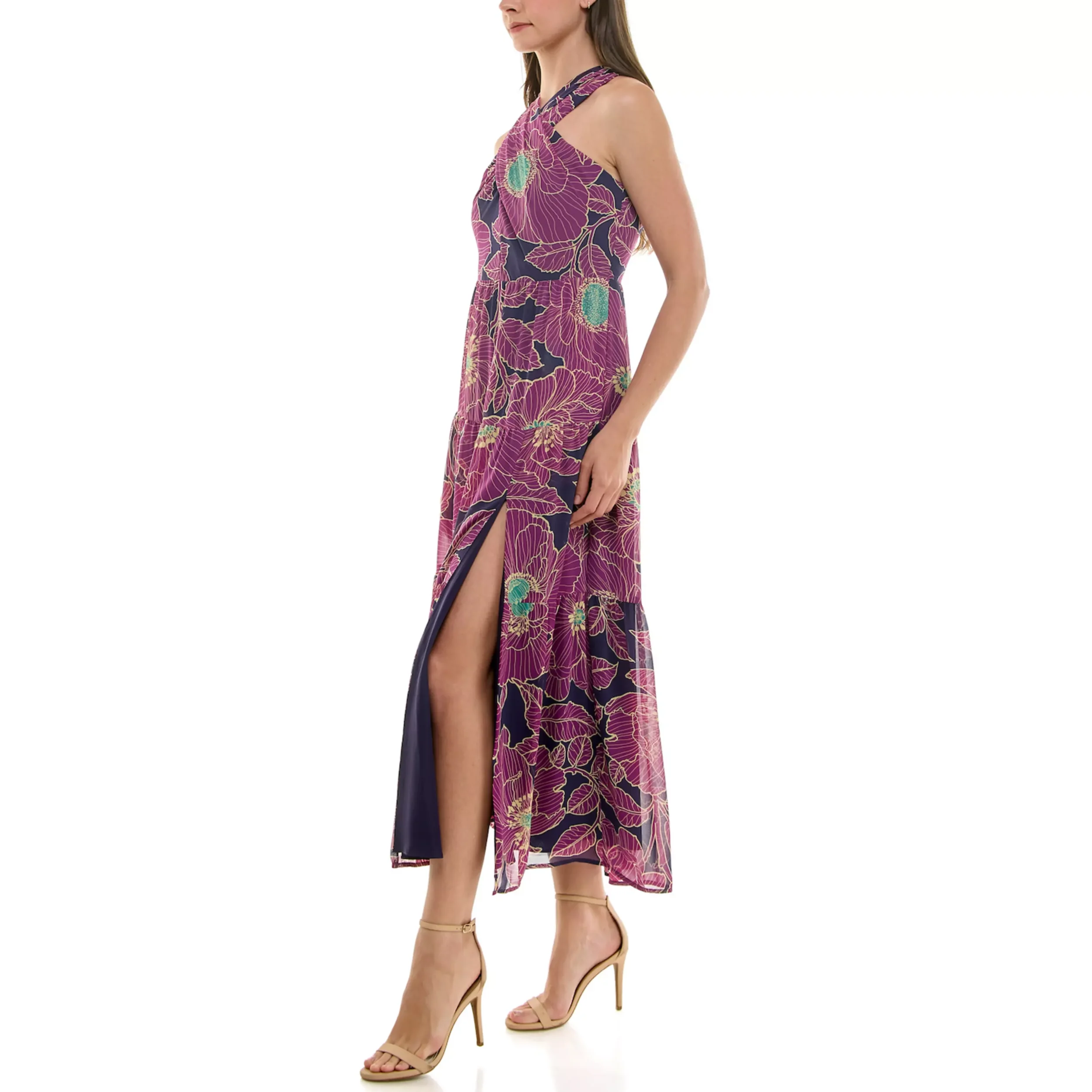 A woman in a sleeveless, floral-printed maxi dress with a high slit, standing in profile against a white background.