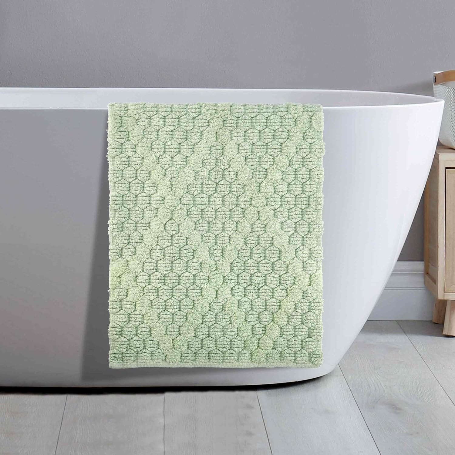 Light green textured towel with geometric pattern hanging over the side of a white bathtub in a bathroom.