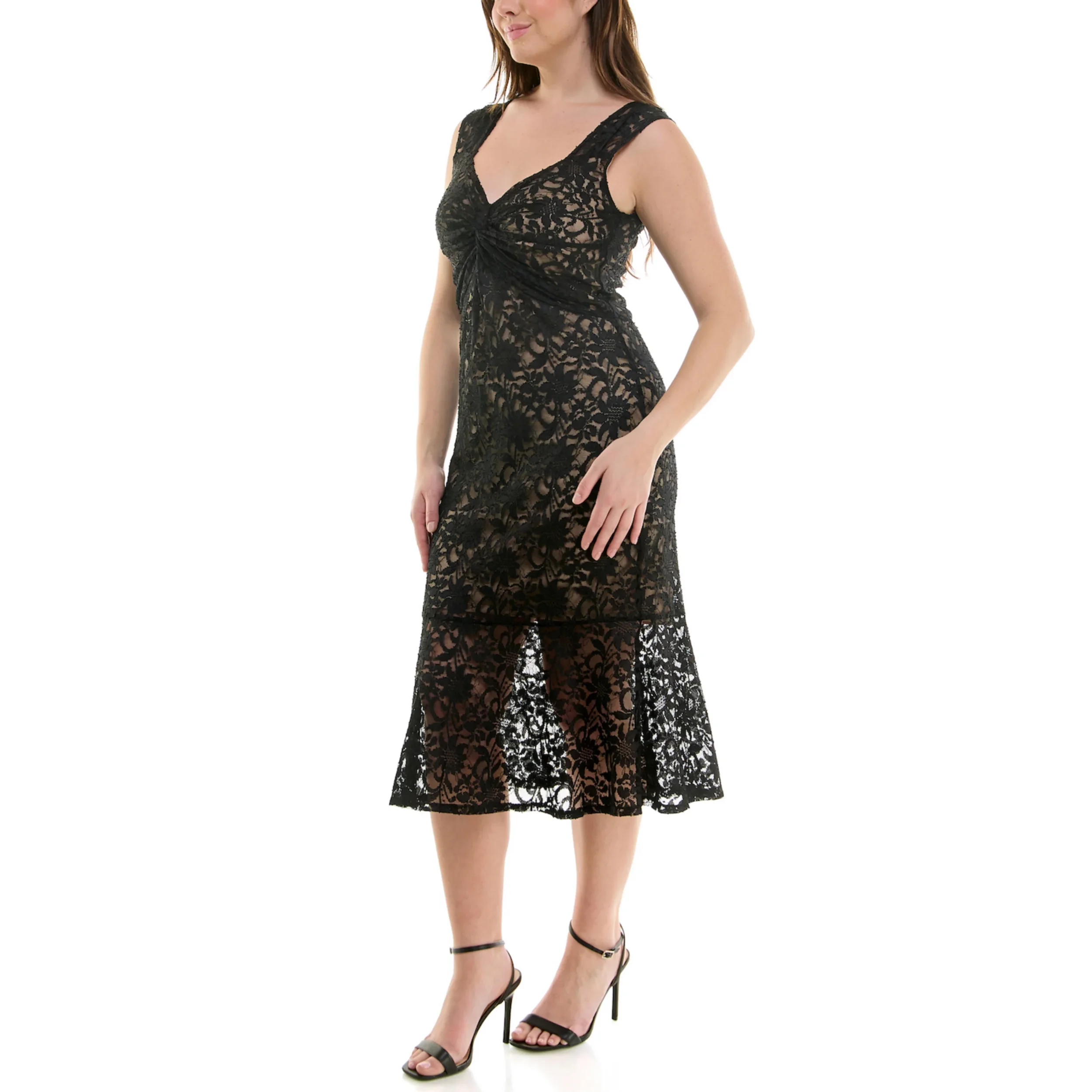 A woman wearing a black lace dress with a floral pattern, sleeveless, with a fitted bodice and an asymmetrical hemline, paired with black high-heeled sandals.