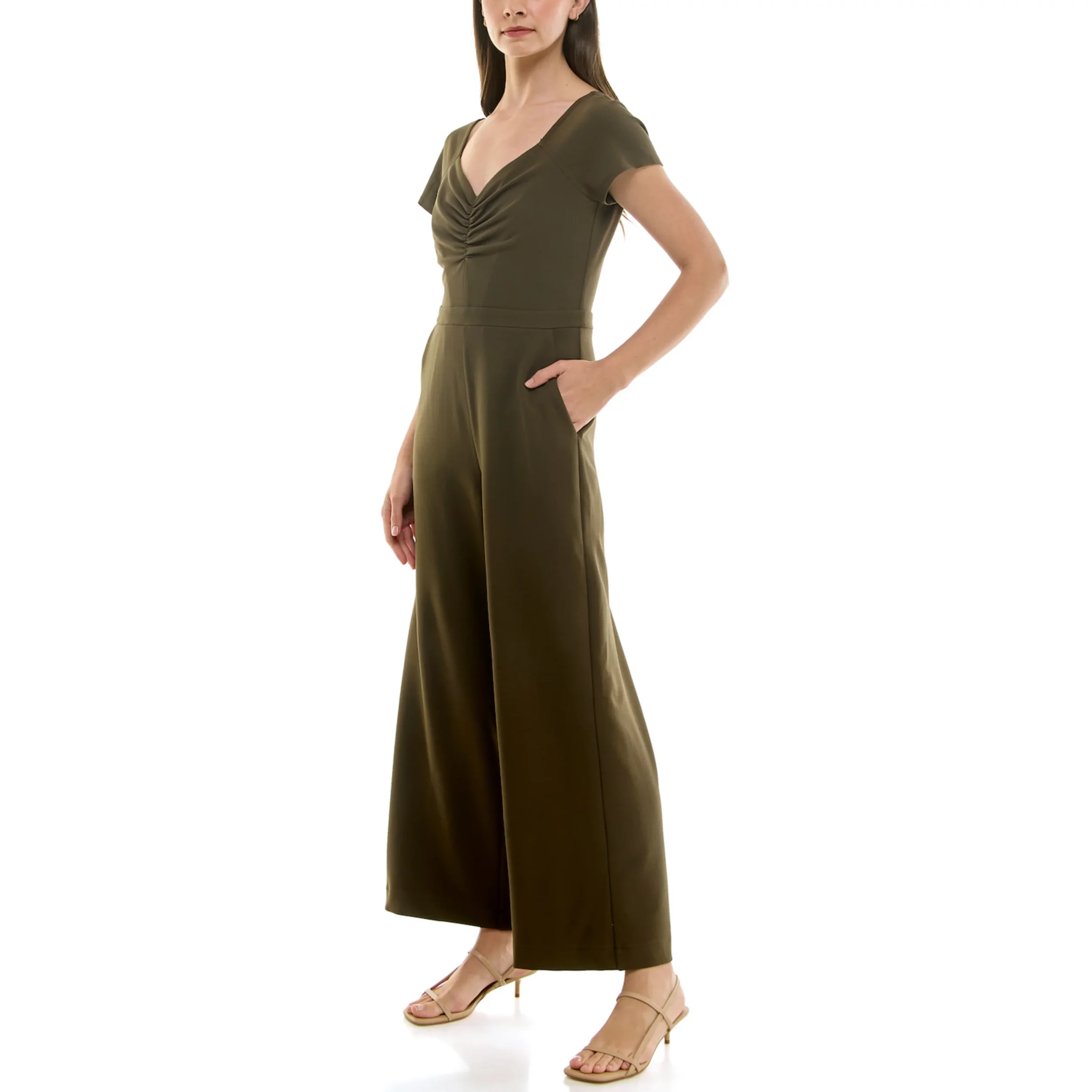 A woman in an olive green jumpsuit with short sleeves, a V-neck, and wide-leg pants, standing with her right hand in her pocket against a white background.