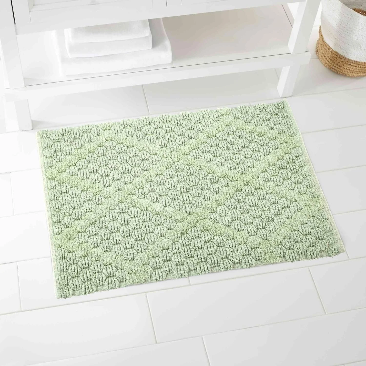 Light green textured rug on white tiled floor in front of a white console table with folded white towels and a woven basket nearby.