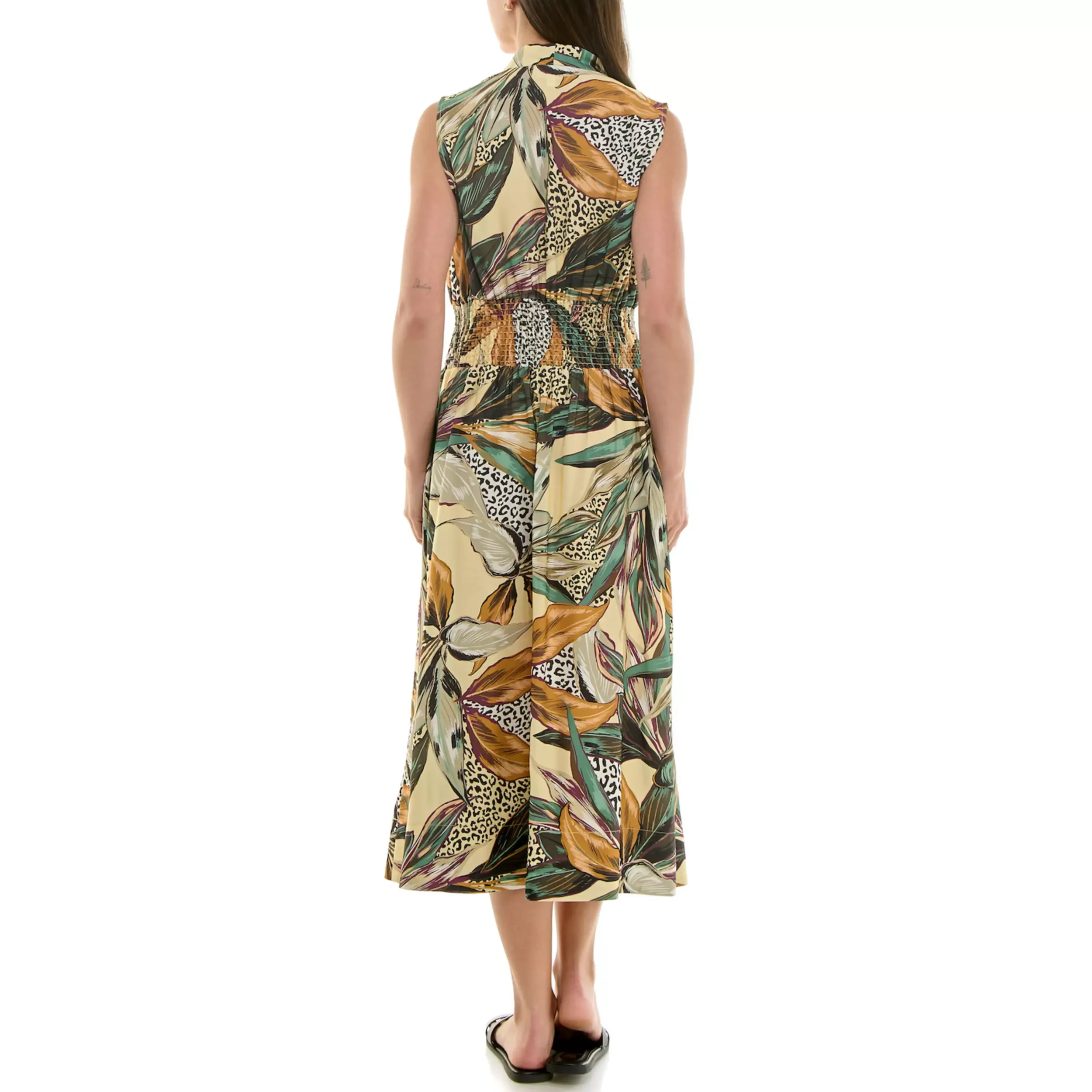 Back view of a woman wearing a sleeveless, long maxi dress with a colorful tropical and animal print pattern, standing on black high-heeled sandals.