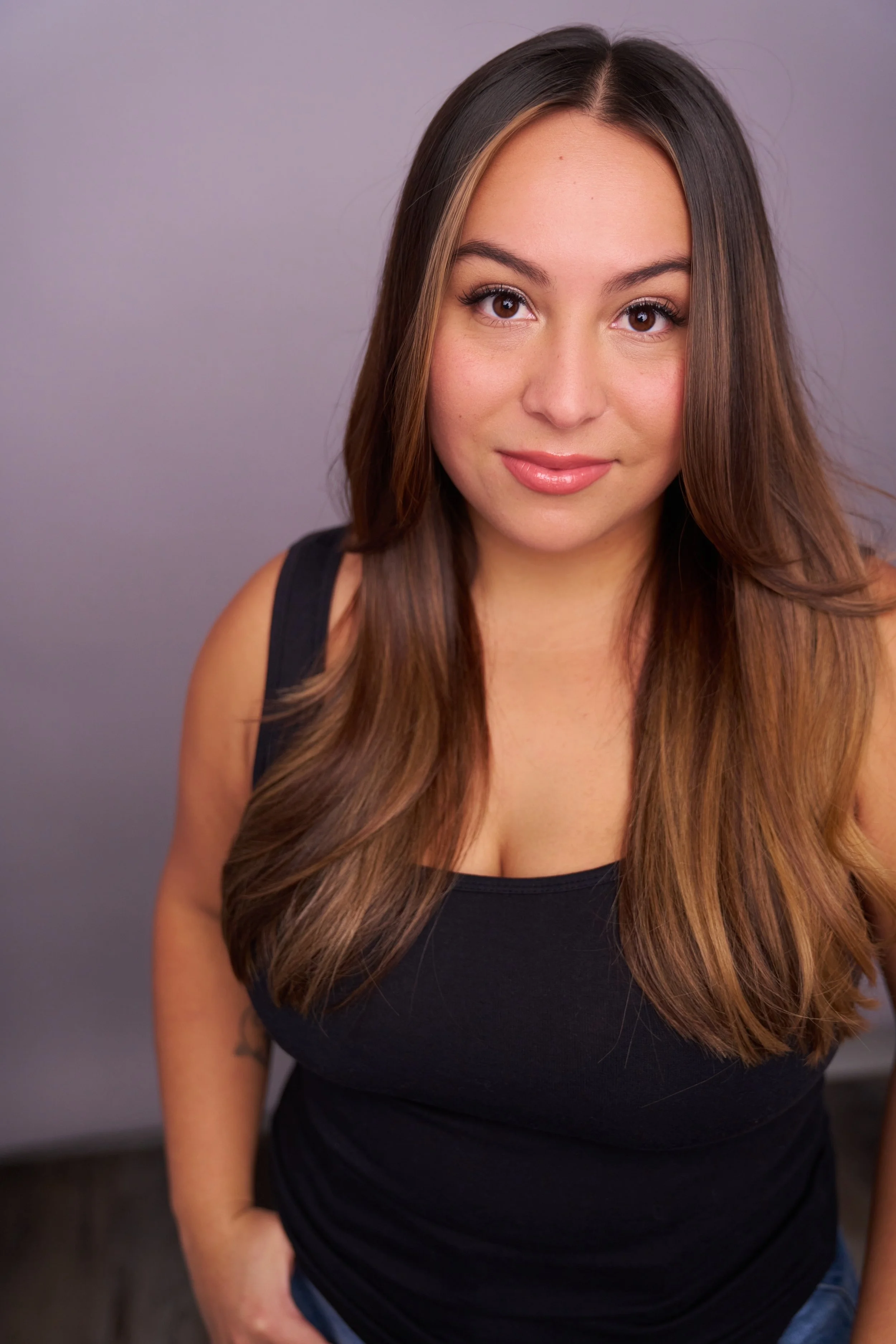 A young woman with long brown hair, wearing a black sleeveless top, looking at the camera with a slight smile.