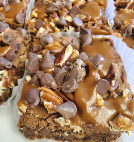 Close-up of a dessert bar topped with chocolate chips, caramel, and chopped nuts.
