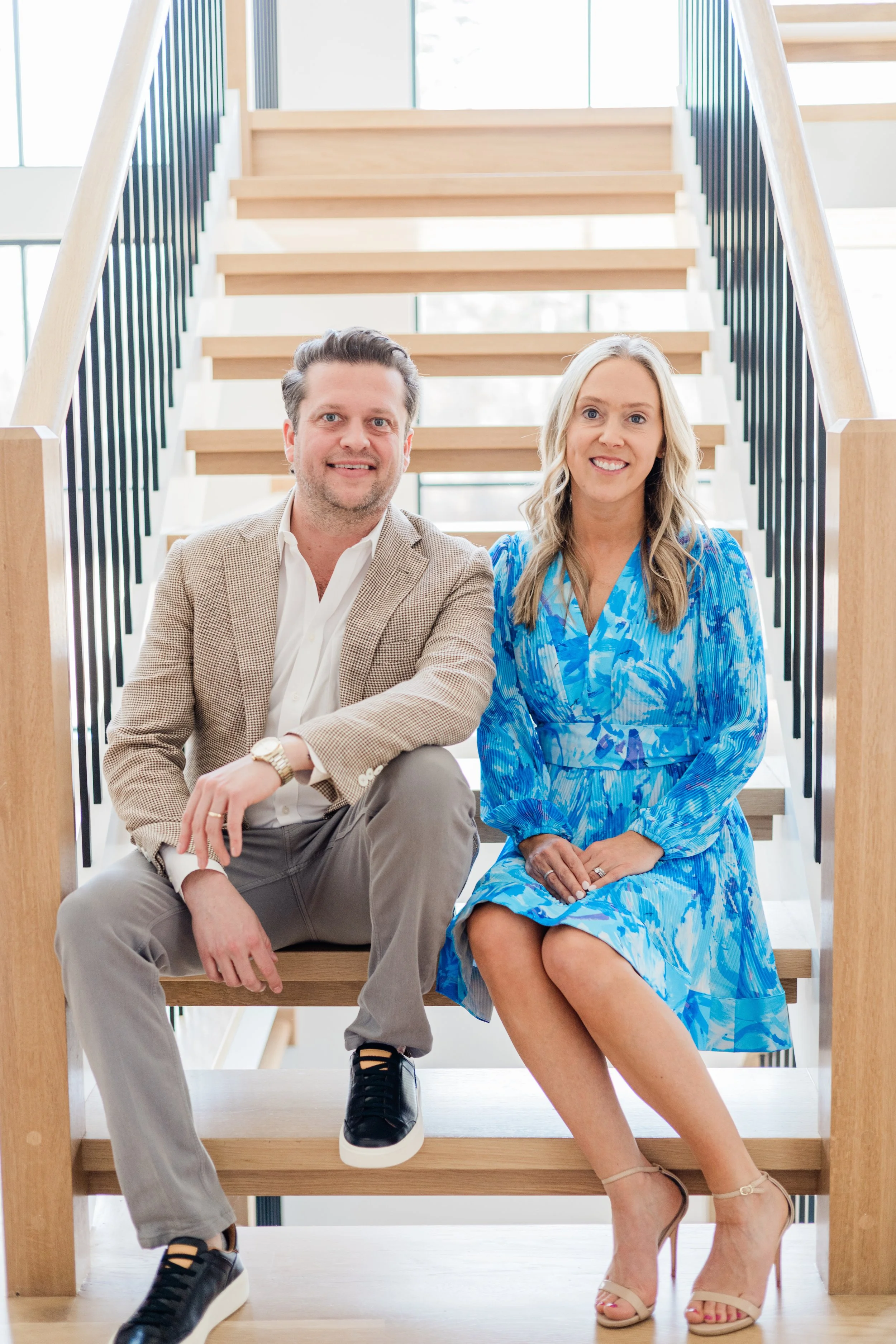 A man and woman sitting on wooden stairs inside a modern building, smiling at the camera.