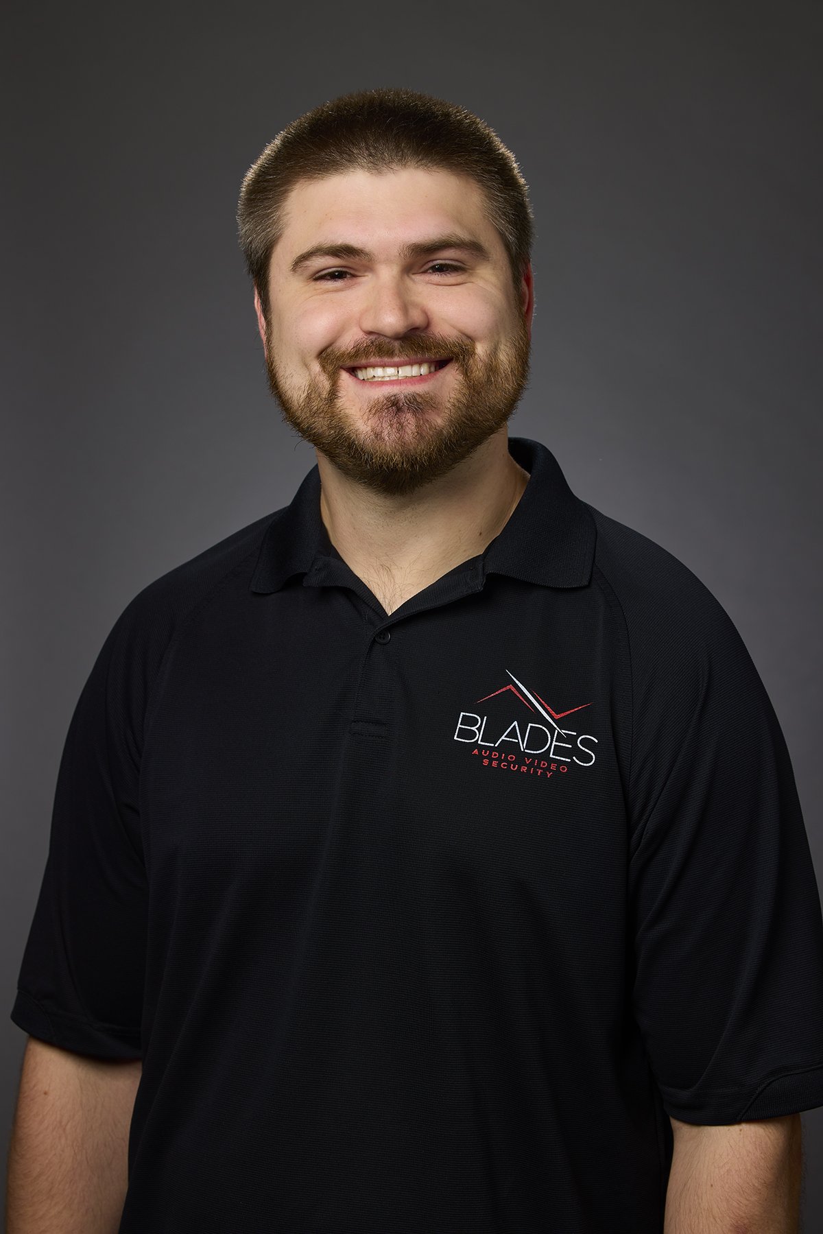 A smiling man wearing a black polo shirt with a logo that reads 'Blades Audio Video Security'.