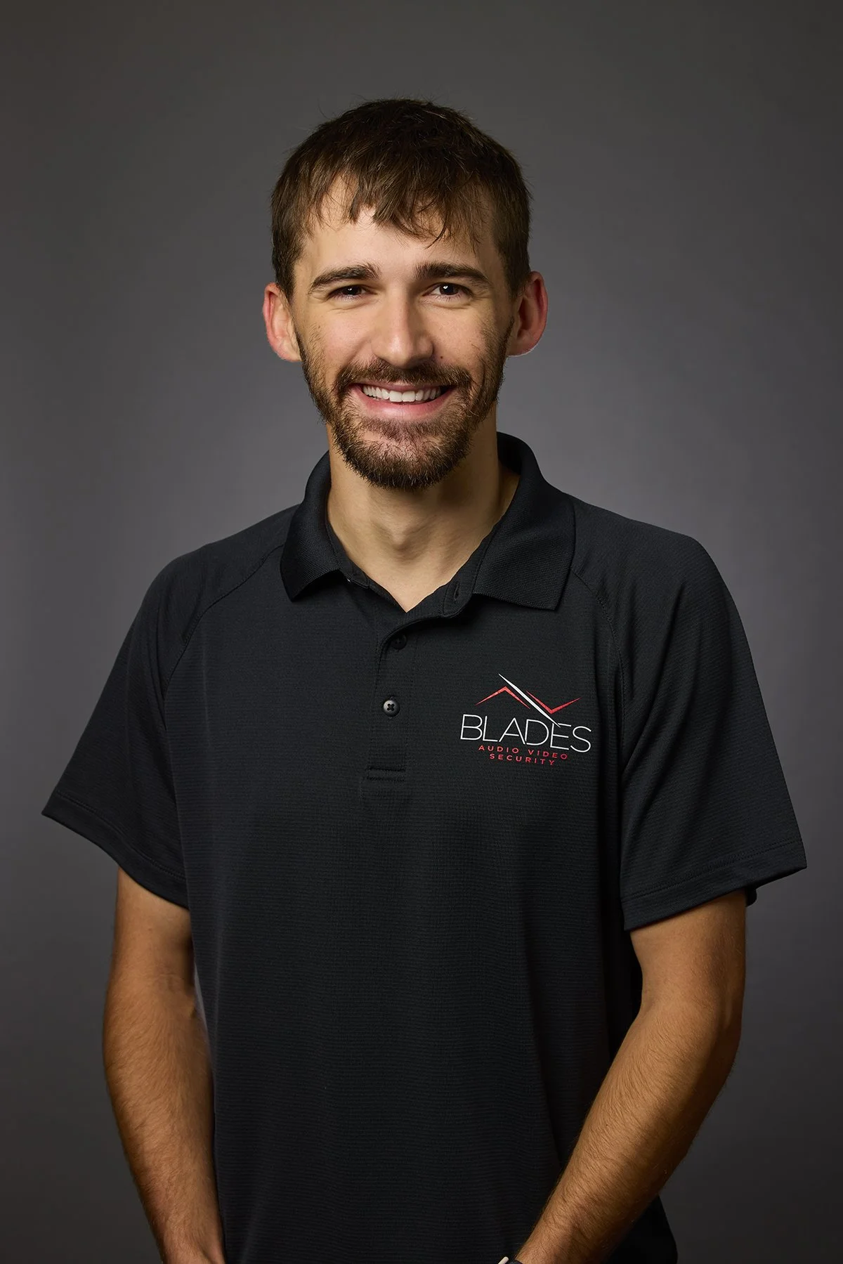 A man wearing a black polo shirt with a 'BLADE' logo, smiling against a gray background.