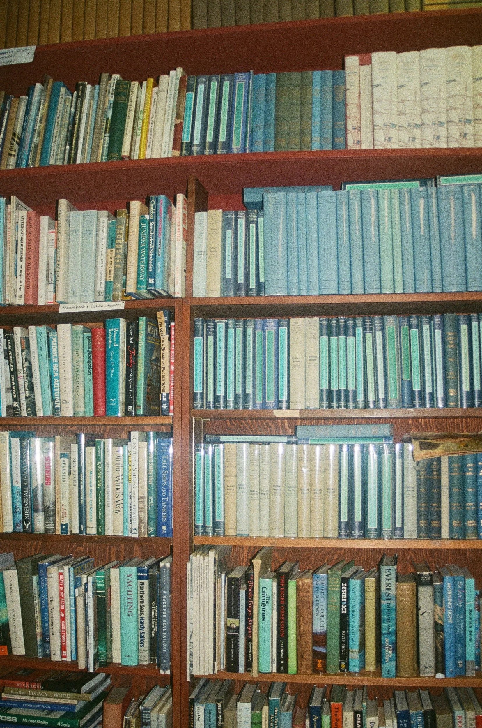 Photo of a wooden bookshelf filled with various books, some with pastel-colored covers, organized in multiple rows and sections.