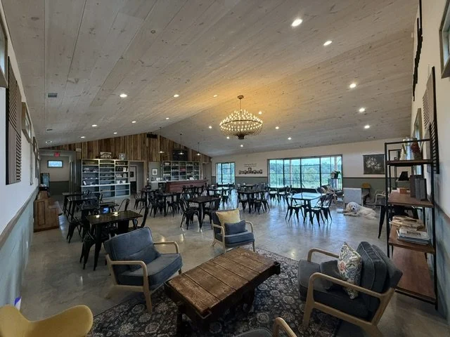 Spacious lounge area with several chairs and tables, decorative wall art, a chandelier, and large windows revealing an outdoor scene.