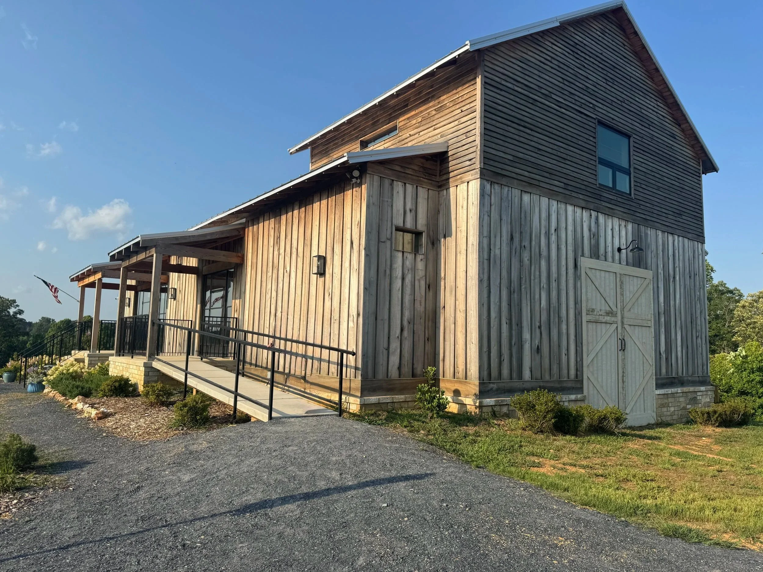 A wooden barn with large double doors, a small window, and a small porch with a railing, under a clear blue sky.