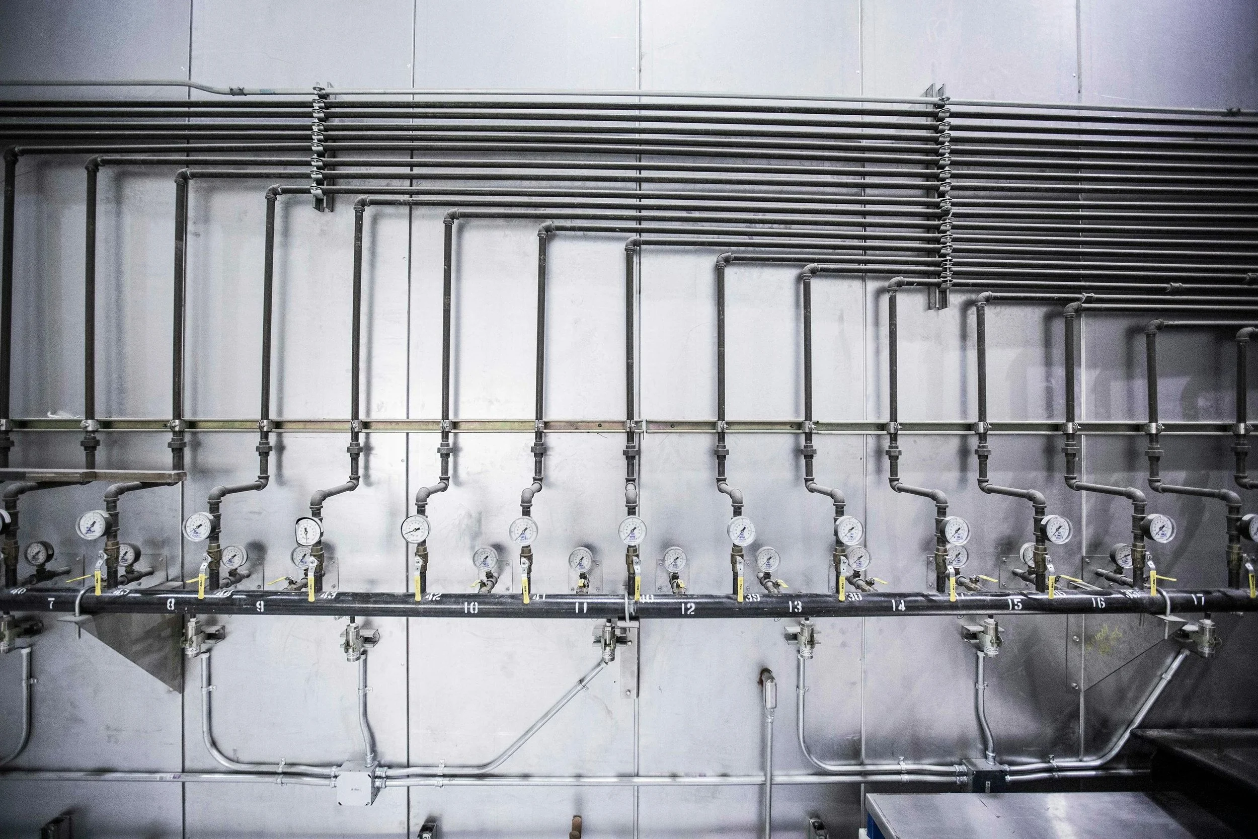 Industrial piping system with gauges and valves mounted on a metallic wall.