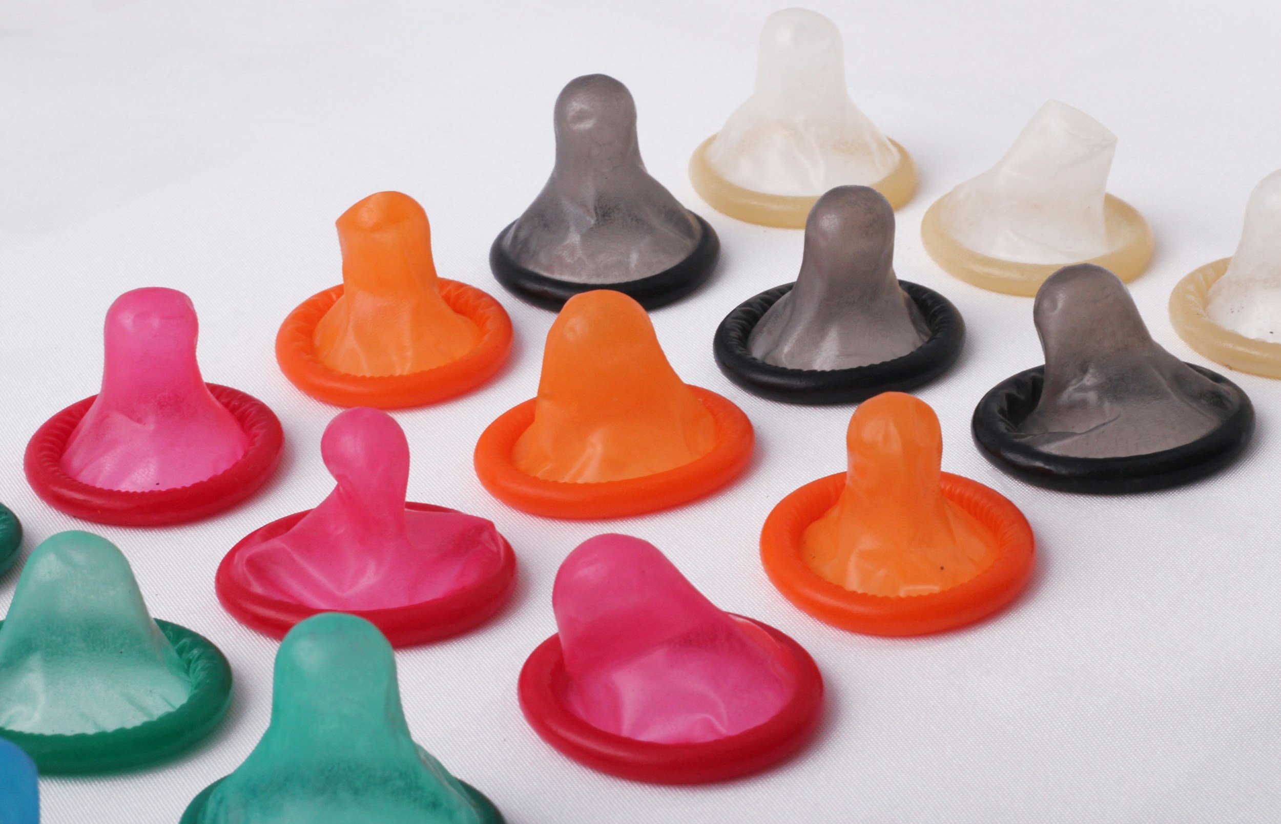 Colorful condoms arranged on a white surface in rows of pink, green, orange, black, and white.