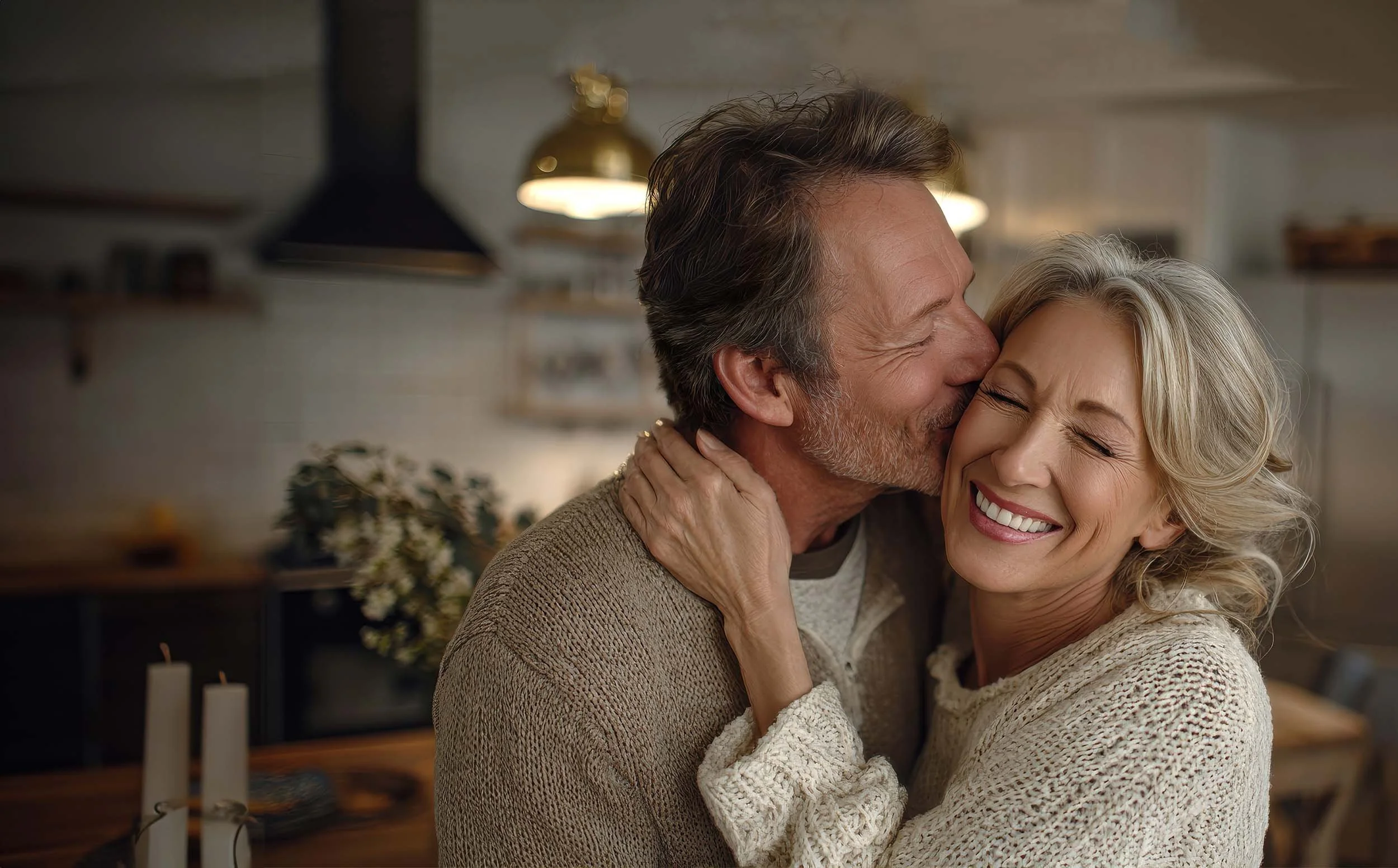 Elderly couple sharing a joyful embrace in a cozy kitchen with warm lighting and candles.