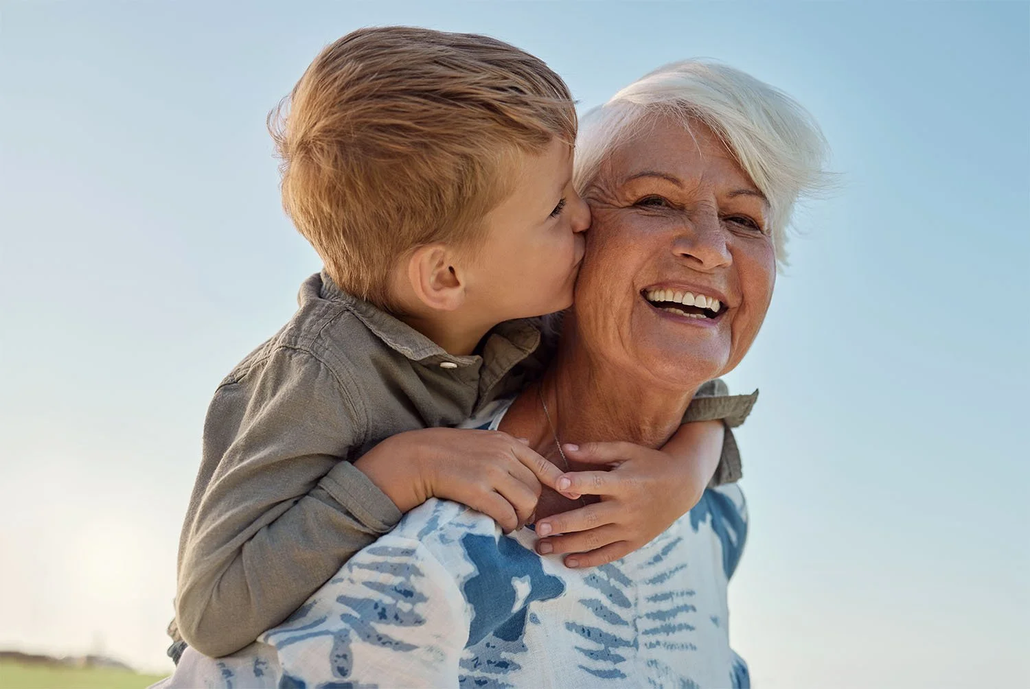 Young boy giving his elderly grandmother a kiss on the cheek outdoors.