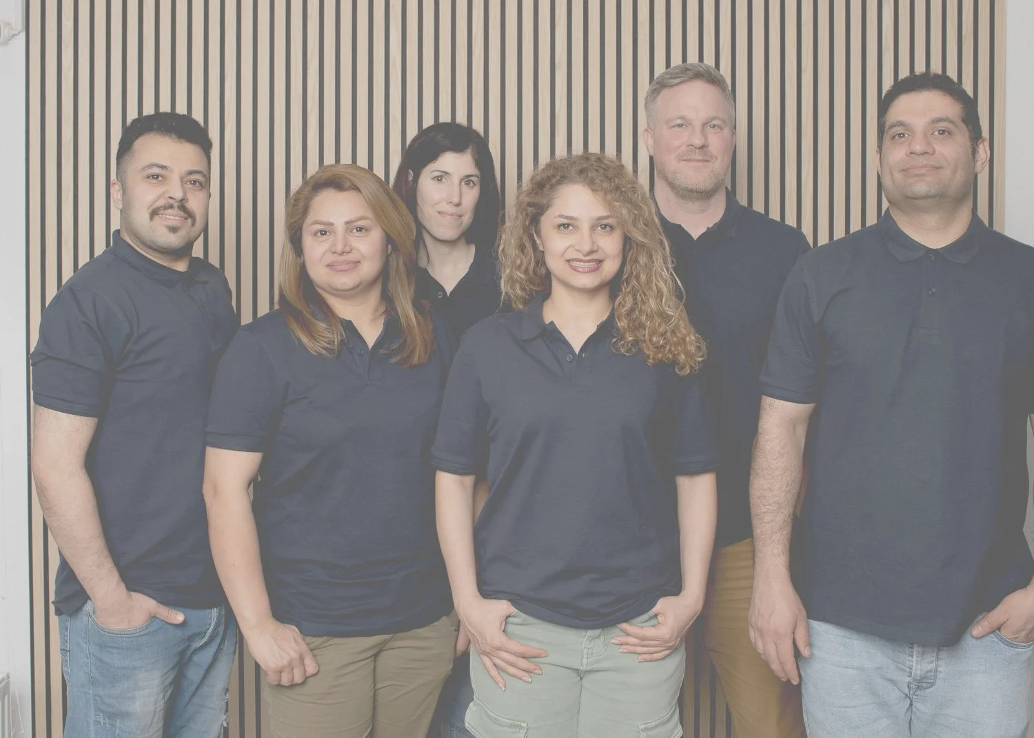 Gruppenfoto von sieben Personen, alle tragen dunkle Polohemden, vor einer Holzvertäfelung.