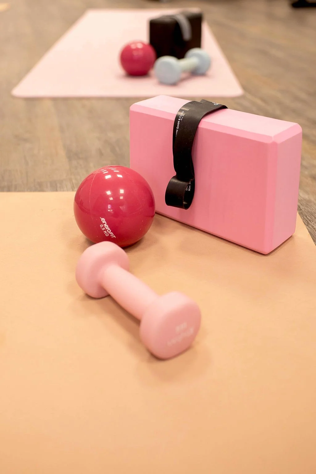 Trainingsgeräte für Pilates im Therapiezentrum Rohan: rosa Kurzhantel, roter Gewichtsball, rosa Yogablock mit Fitnessband auf einer Trainingsmatte