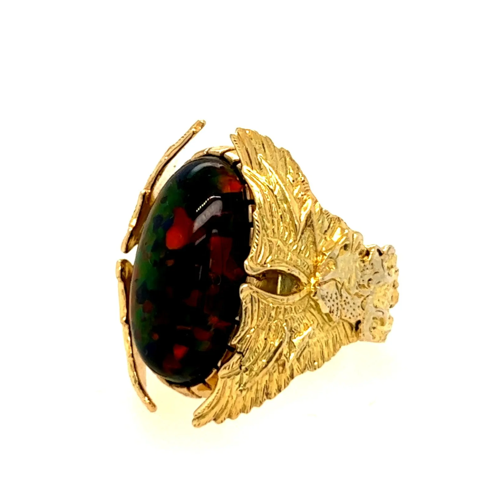 Close-up of a gold ring with an oval black gemstone, designed with wing and eye motifs, against a white background.