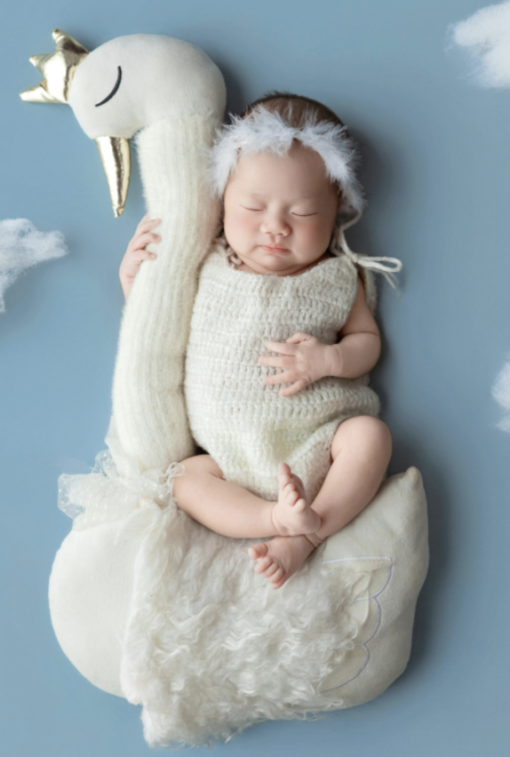 Cute baby dressed as a Christmas elf, lying on a cloud-shaped pillow with a plush unicorn-themed sock and a fluffy tail attached, surrounded by soft clouds on blue background.