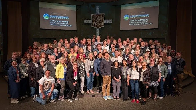Group of diverse people gathered on stage at a conference, with a large cross and two screens behind them displaying the event name, for the 135th Annual Meeting of the Keystone Conference.