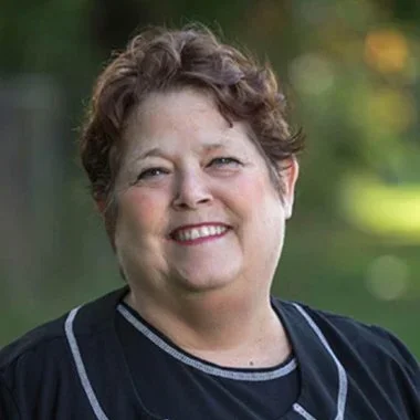 Portrait of a smiling woman with short curly hair outdoors.