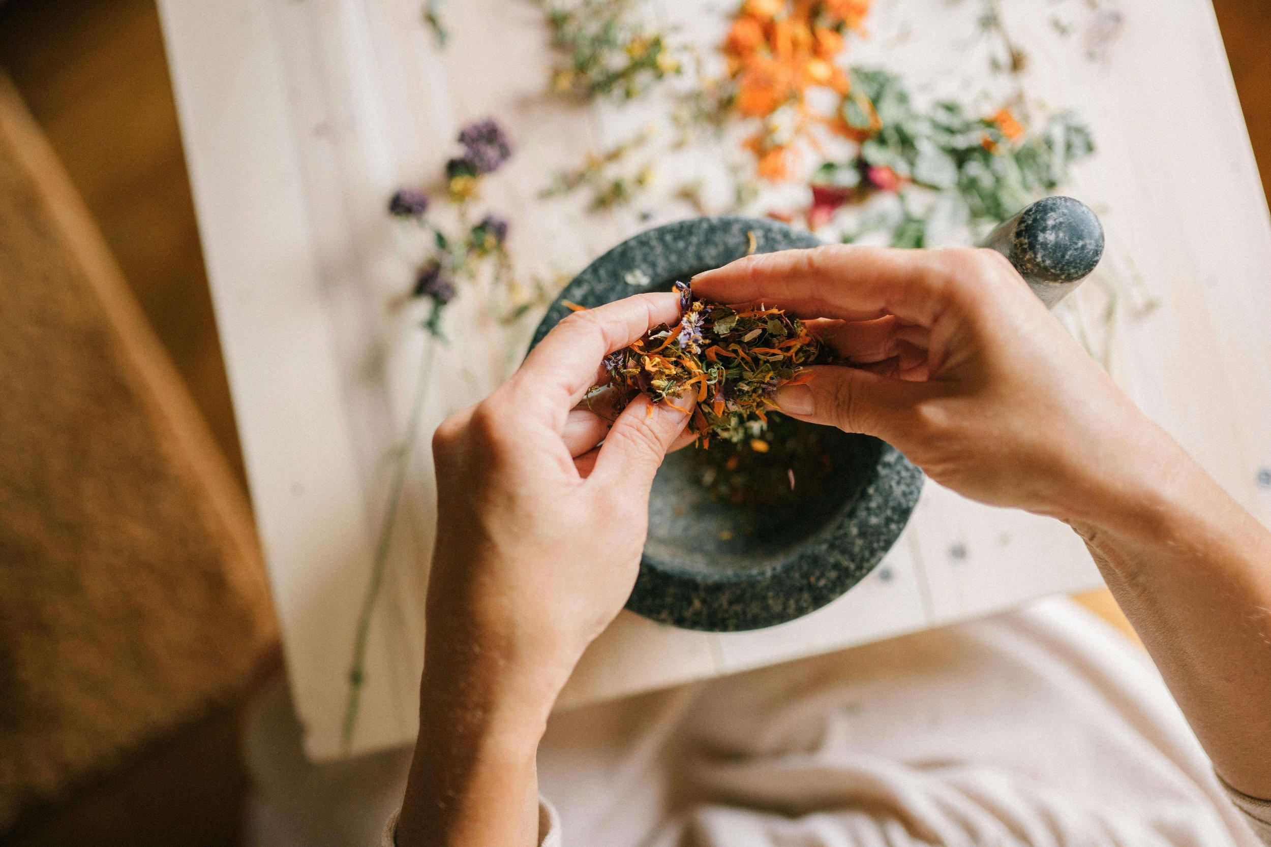 A holistic doctor putting herbs into a mortar and pestle. This is part of what care with functional medicine looks like. While your St. Louis based doctor will prescribe western medicine as needed. They will also support your health through herbs.
