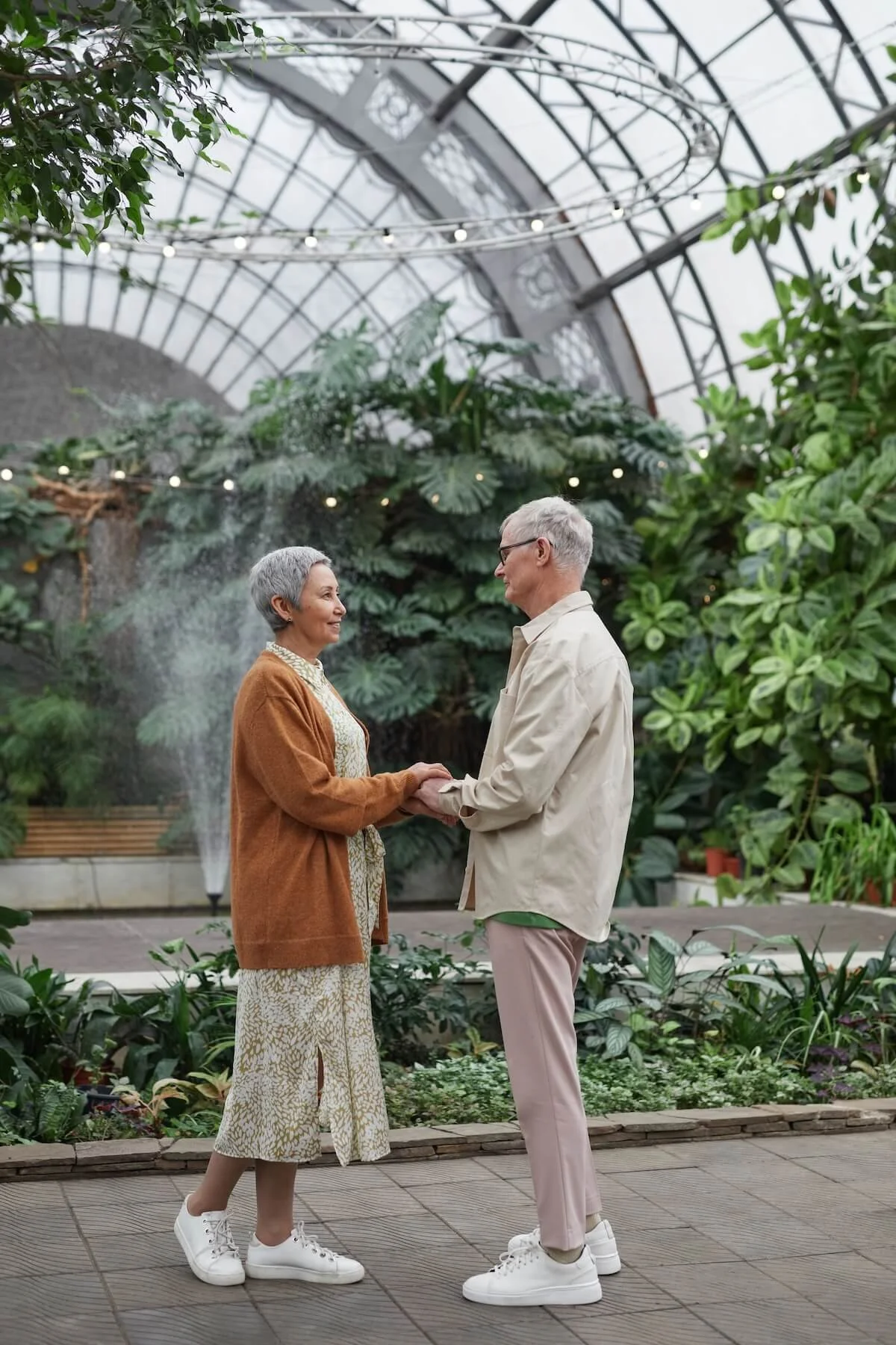 An older couple holds hands and smiles at each other inside a lush botanical garden, reflecting the lasting connection and renewed closeness that couples counseling in St. Louis helps partners build with a couples counselor in St. Louis.