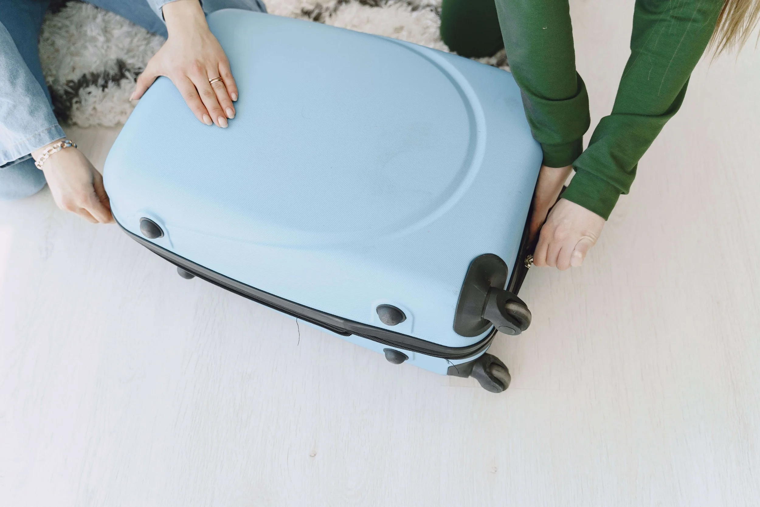 Two women close a light blue suitcase before a trip. Are unmet expectations turning your vacations into a source of tension rather than joy? Couples counseling in St. Louis, MO offers support for managing disappointment as a couple.