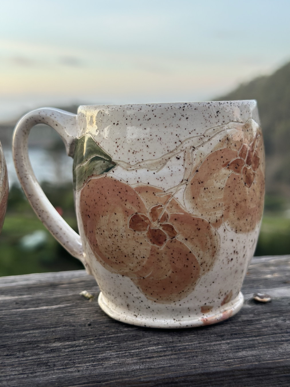 Close-up of a ceramic mug with a floral design, set on a wooden surface outdoors during sunset.