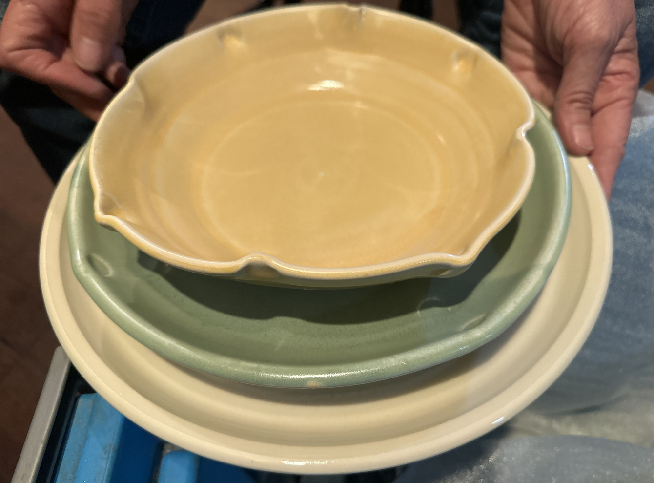 Stack of three ceramic bowls in yellow, green, and beige colors being held by a person.