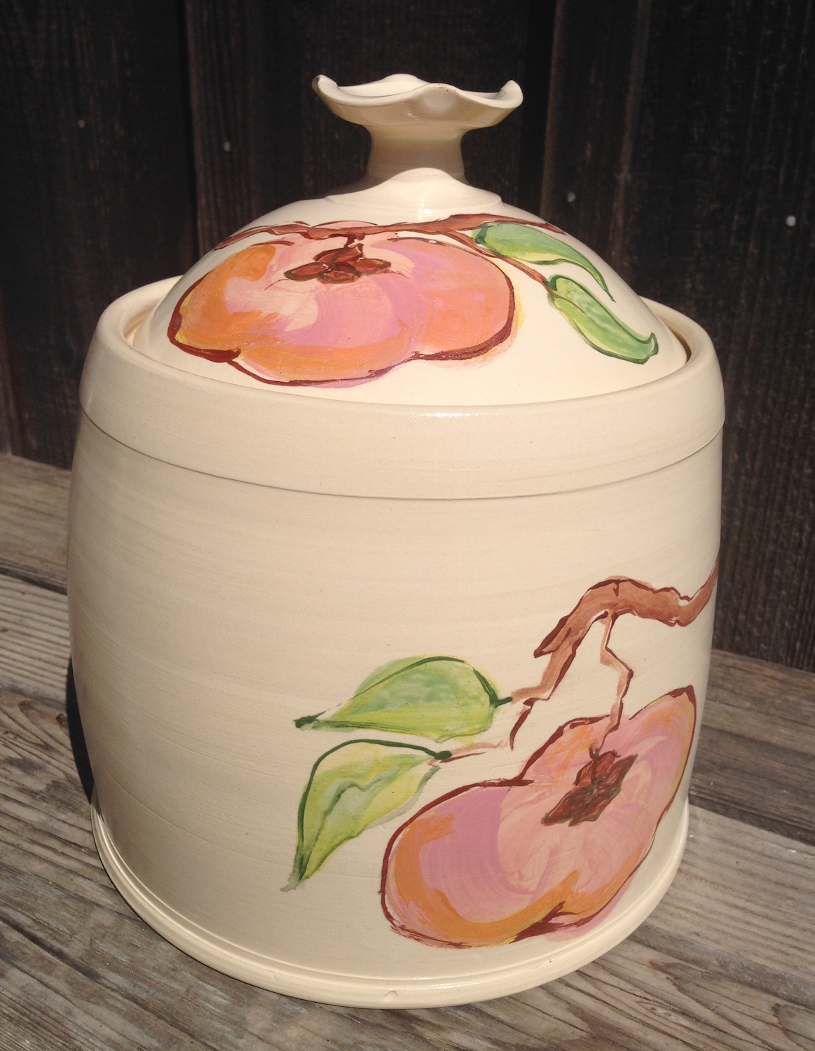 Ceramic container with a painted peach and leaf design on a wooden surface.