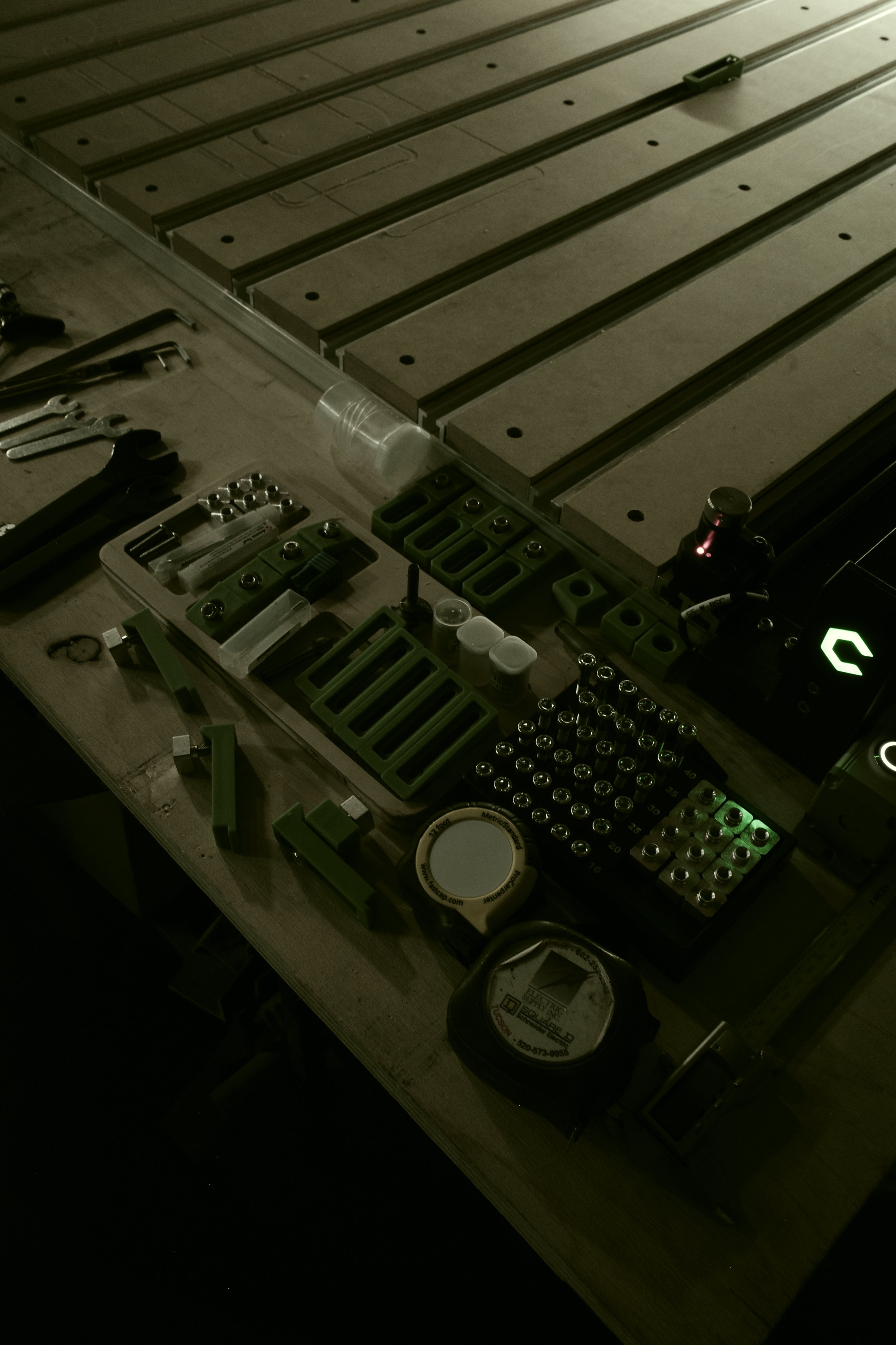 A workbench with tools, small containers, and mechanical parts, with a partially assembled metal structure in the background.