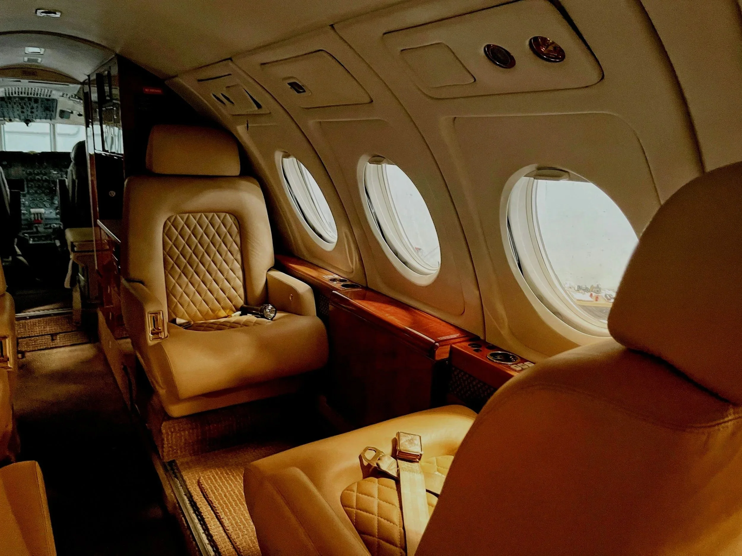 Interior of a private jet with beige leather seats, wooden accents, and multiple airplane windows.