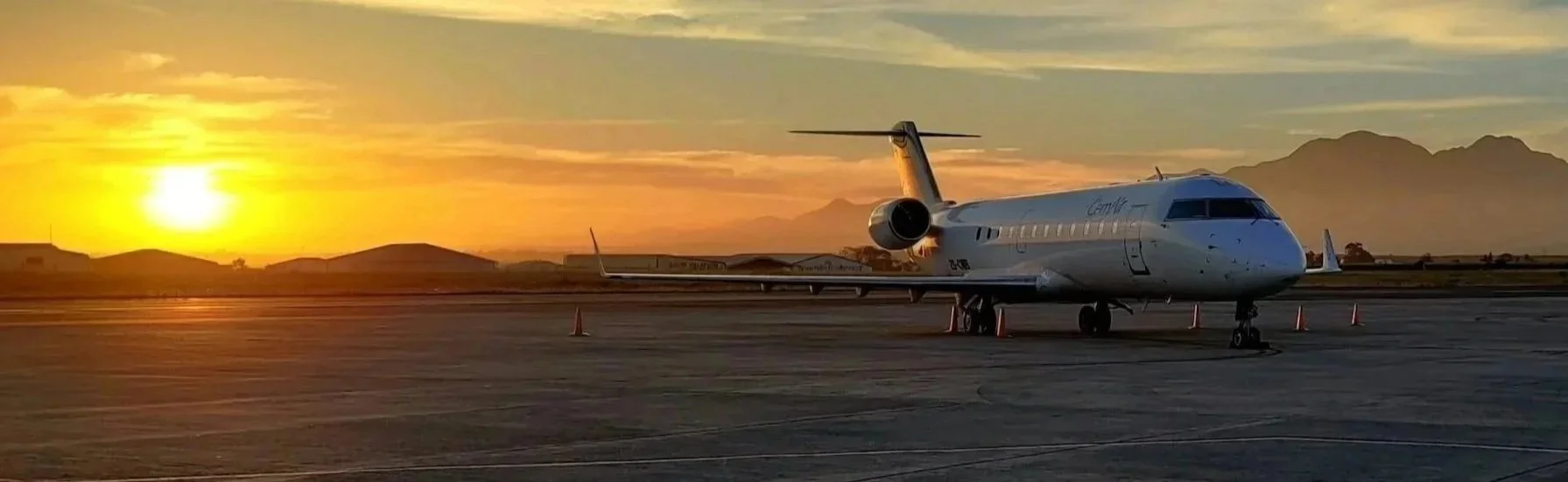 Private jet parked on the tarmac at sunset with mountains in the distance.