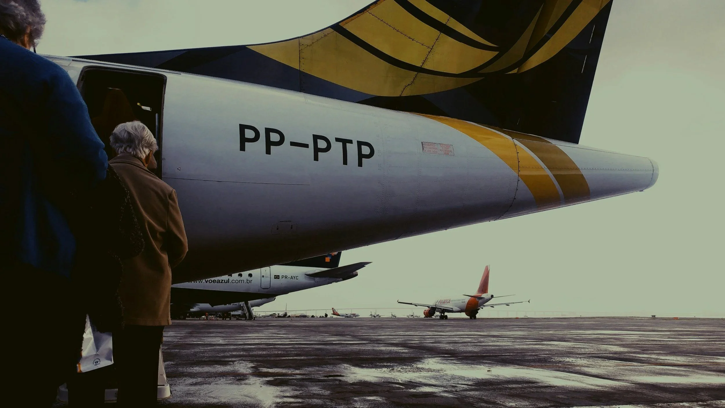 People boarding a large airplane on an airport tarmac, with several other planes parked in the background.