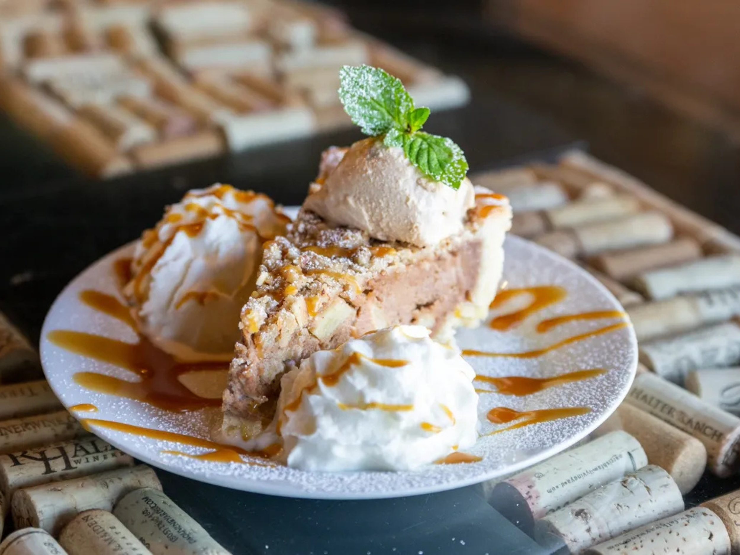 Slice of caramel apple dessert with ice cream, whipped cream, caramel drizzle, and mint leaf on a white plate
