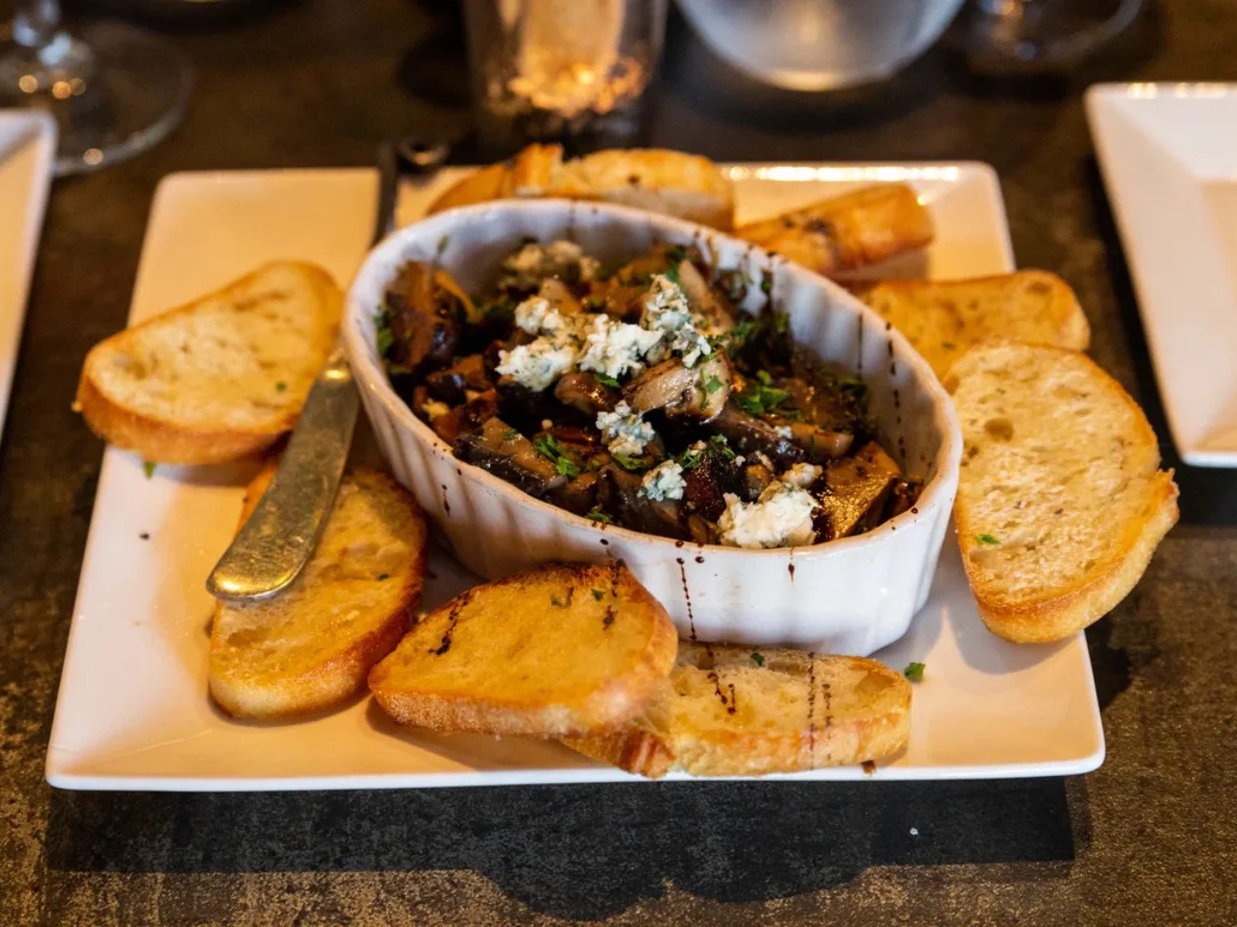Baked bread slices surrounding a dish with cooked mushrooms, herbs, and crumbles of blue cheese.