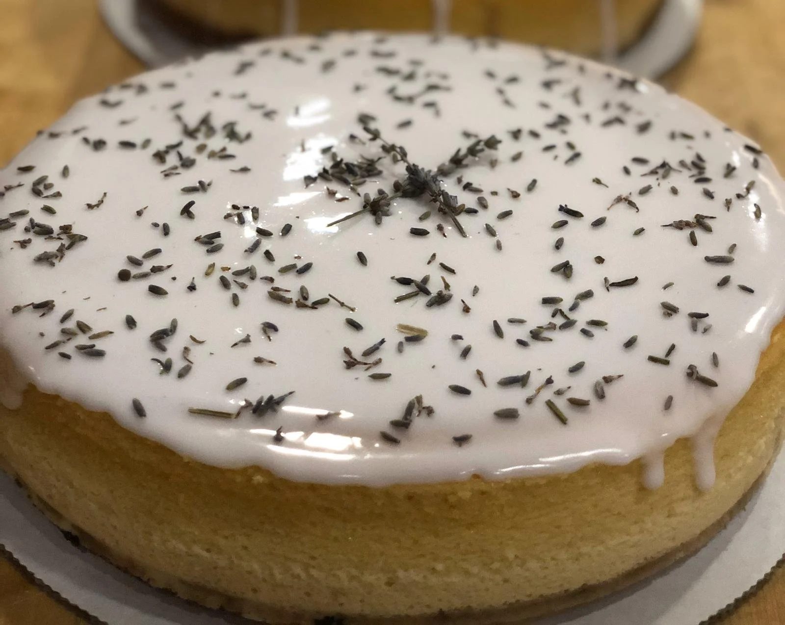 Close-up of a round lemon cake with white icing and sprinkled lavender flowers on top.