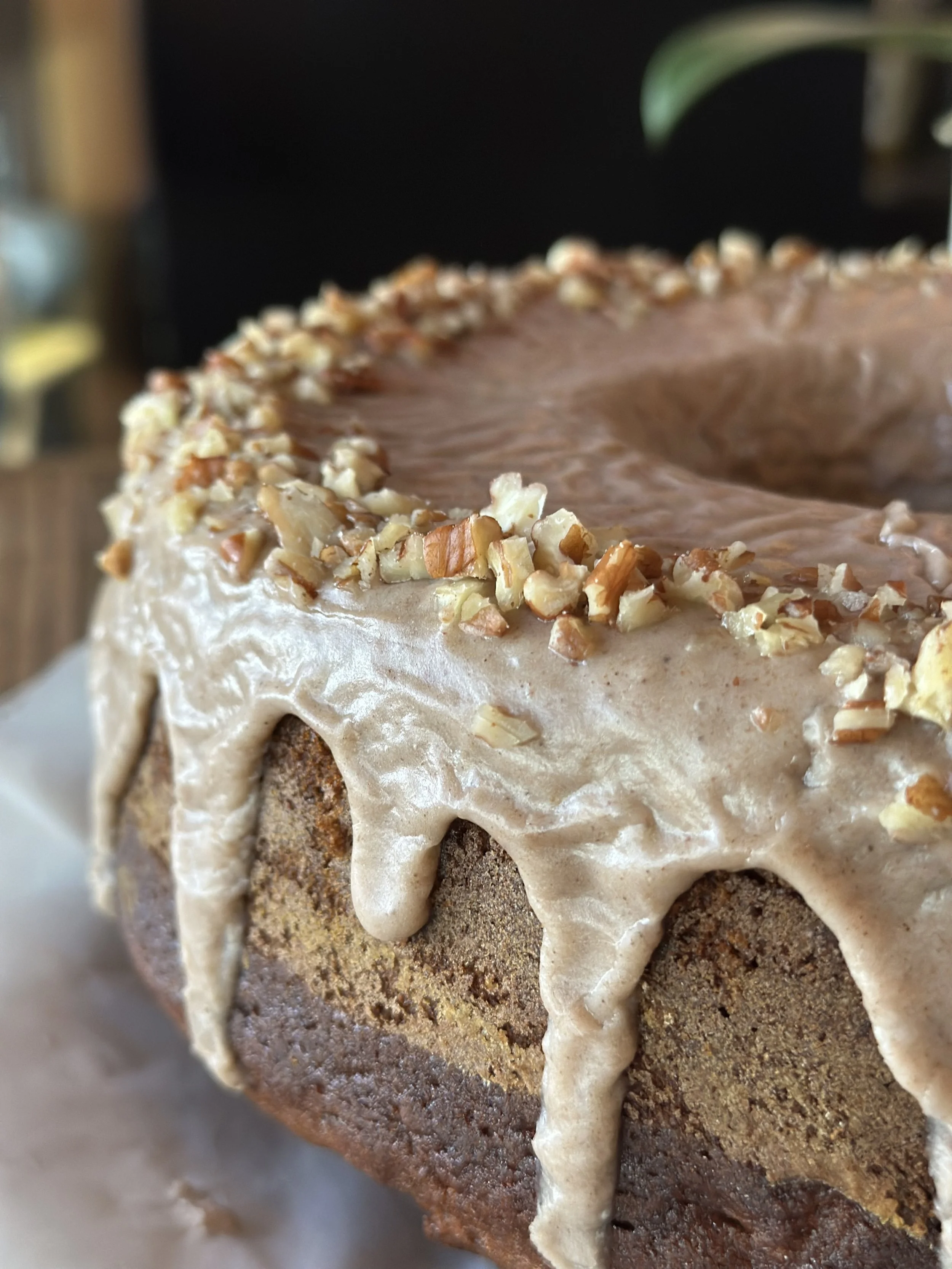 Close-up of a pumpkin-shaped cake with caramel or beige frosting, topped with chopped nuts around the top edge.