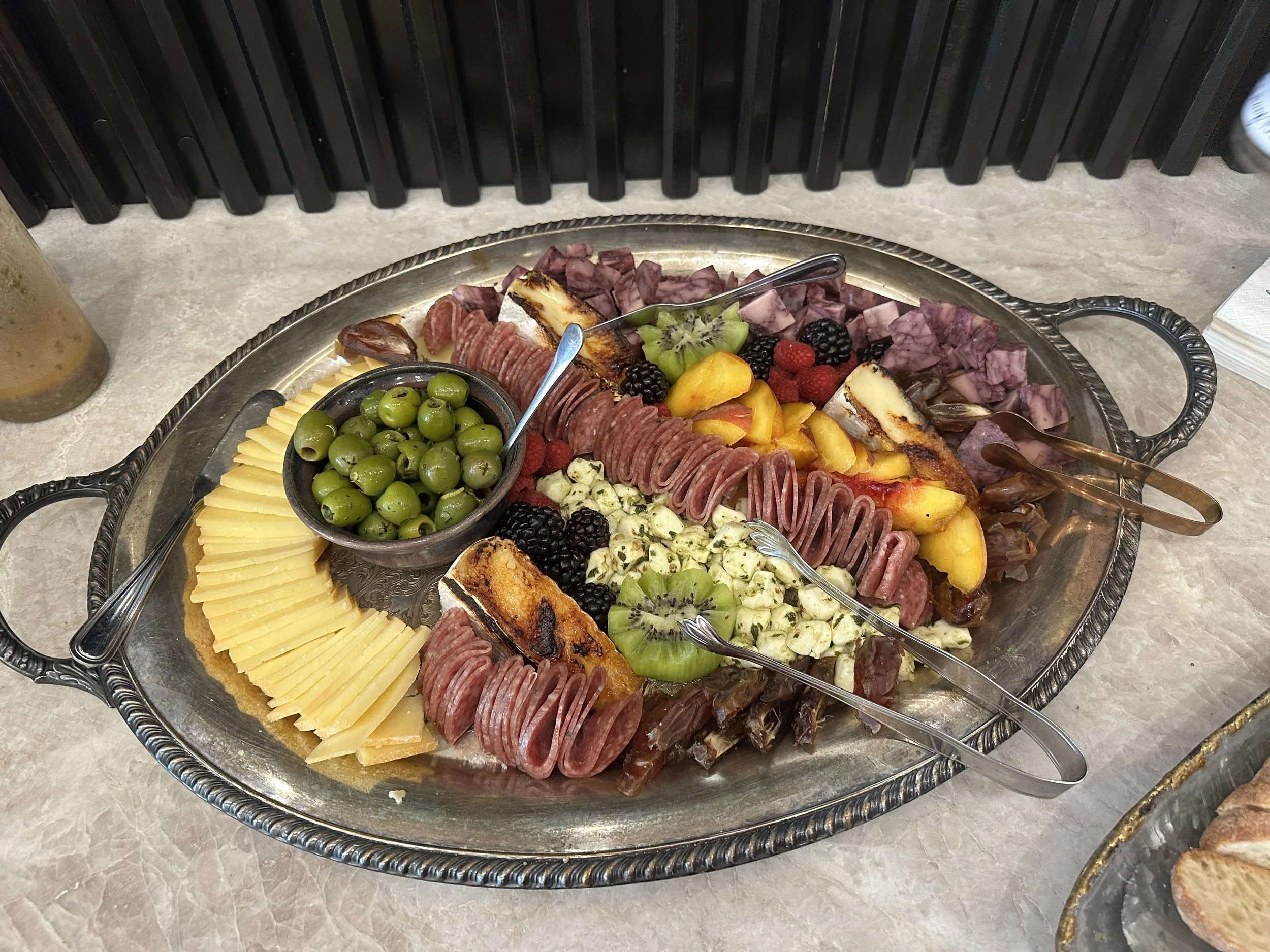 Charcuterie platter with assorted cheeses, sliced cured meats, fresh fruits like kiwi, peaches, strawberries, blackberries, and green olives.