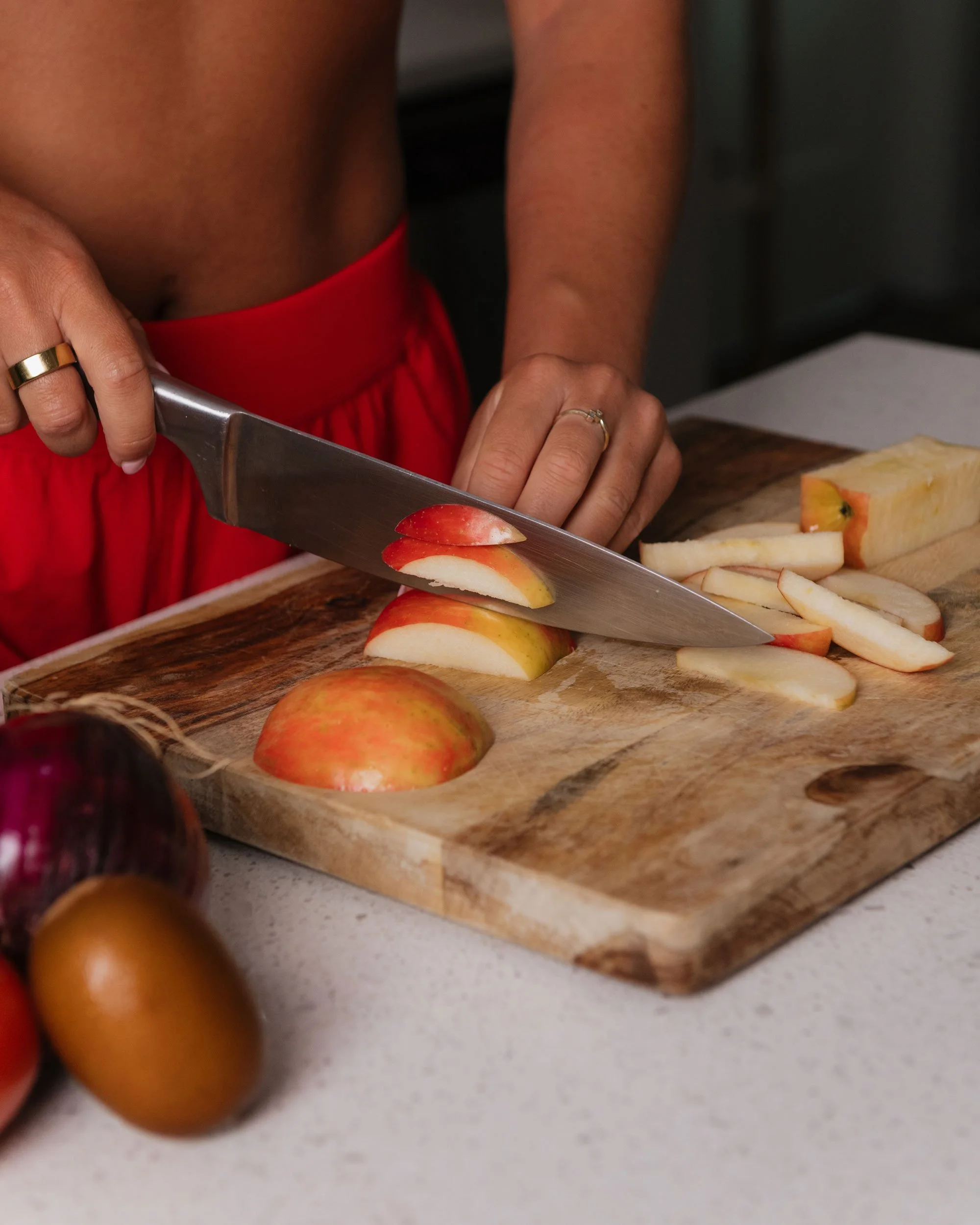 Person slicing an apple on a wooden cutting board with other fruits nearby.