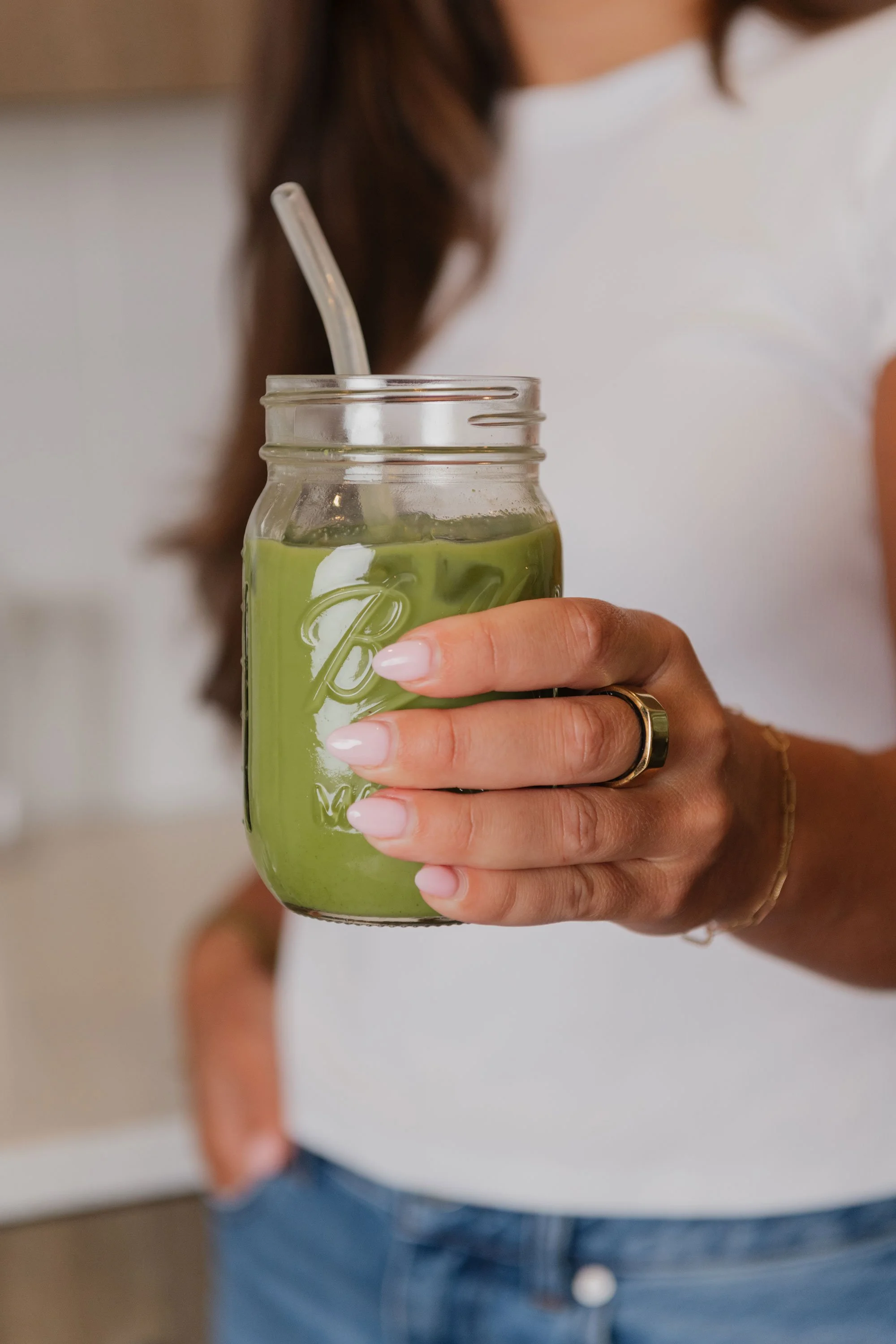 A woman holding a mason jar with a green smoothie and a straw.