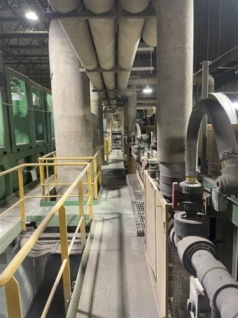 Industrial factory floor with pipes, machinery, and safety railings.