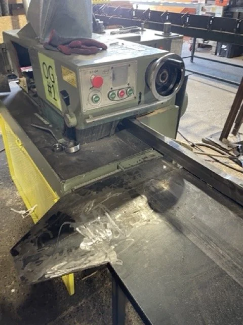 A large industrial metal cutting or grinding machine with a damaged or burned metal piece in front of it, in an industrial workshop setting.