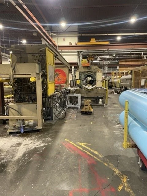 Industrial factory floor with machinery, pipes, and a large roll of blue material on the right side.
