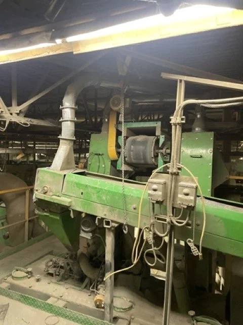 Close-up of a large green industrial machine, showing belts, wires, and pipes in a factory setting.