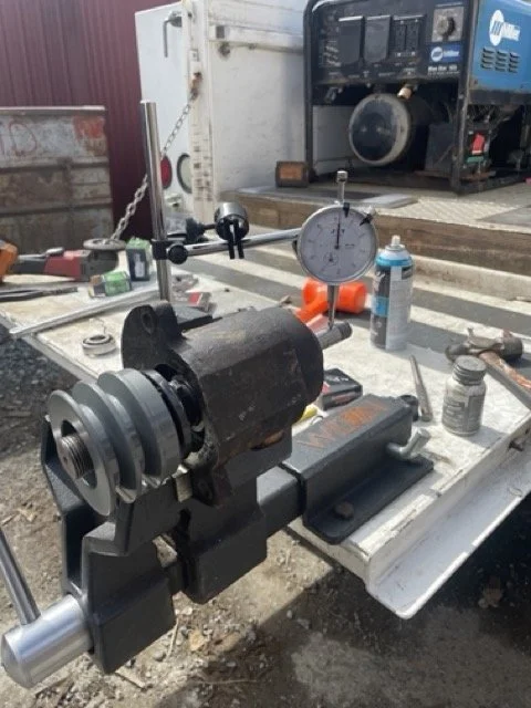 A rotating metal piece mounted on a workbench with tools and measuring equipment nearby, outdoors with a generator in the background.