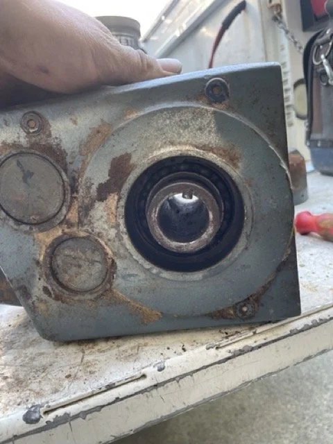 A rusted metal speaker with a large central cone and two smaller circular areas, placed on a workbench with tools in the background.