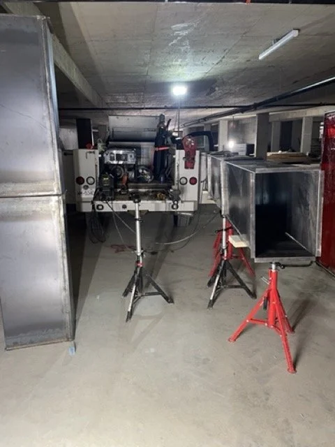 Underground parking garage with equipment set up, including a machine or generator on a stand, metal containers, and red sawhorses.
